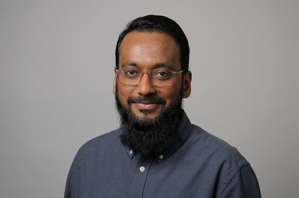 Portrait of Hasan Baig wearing a blue button up dress shirt.