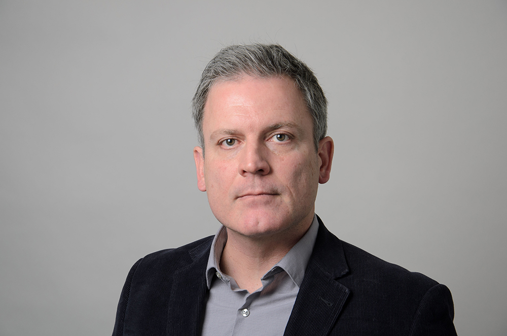 Portrait of Augusto Buchweitz wearing a blazer and gray collared shirt.