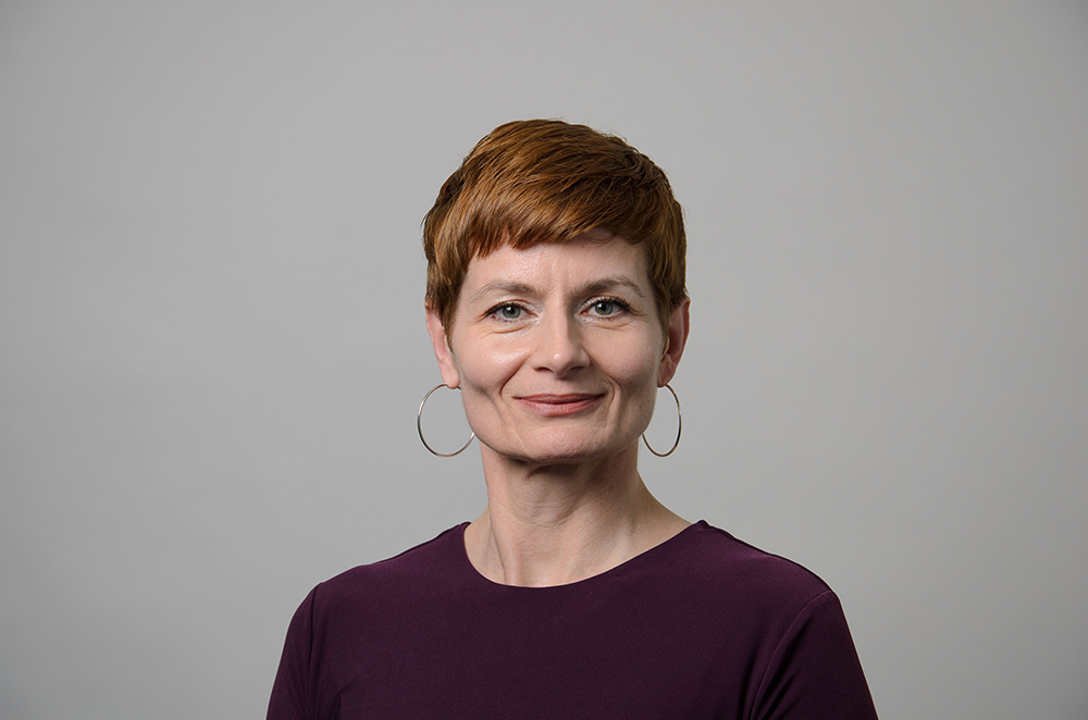 Portrait of Annamaria Csizmdia wearing gold hoop earrings and a maroon shirt.