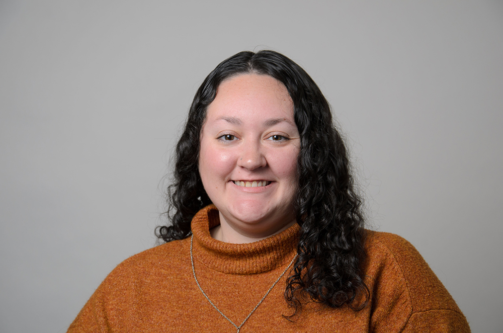 Portrait of Abby Manente wearing a dark orange turtleneck sweater.