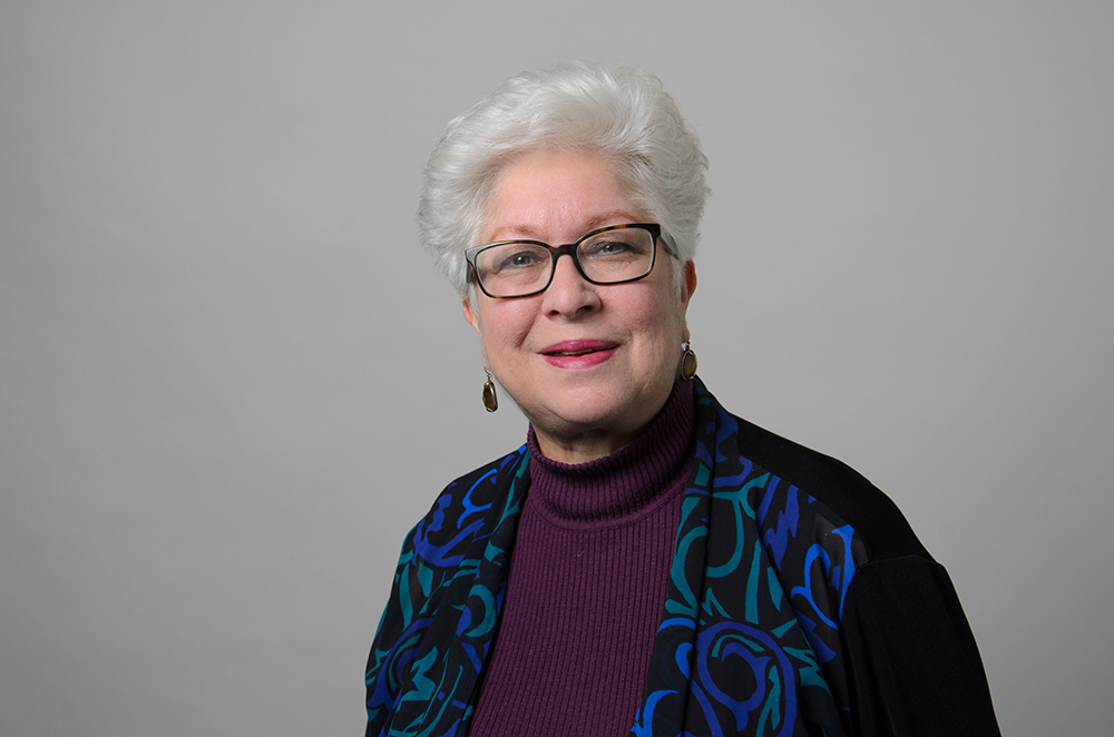 Portrait of Judy Stewart wearing a purple turtleneck and a patterned blazer.