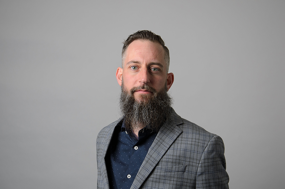 Portrait of Aris Ristau wearing a gray plaid blazer and blue collared shirt.