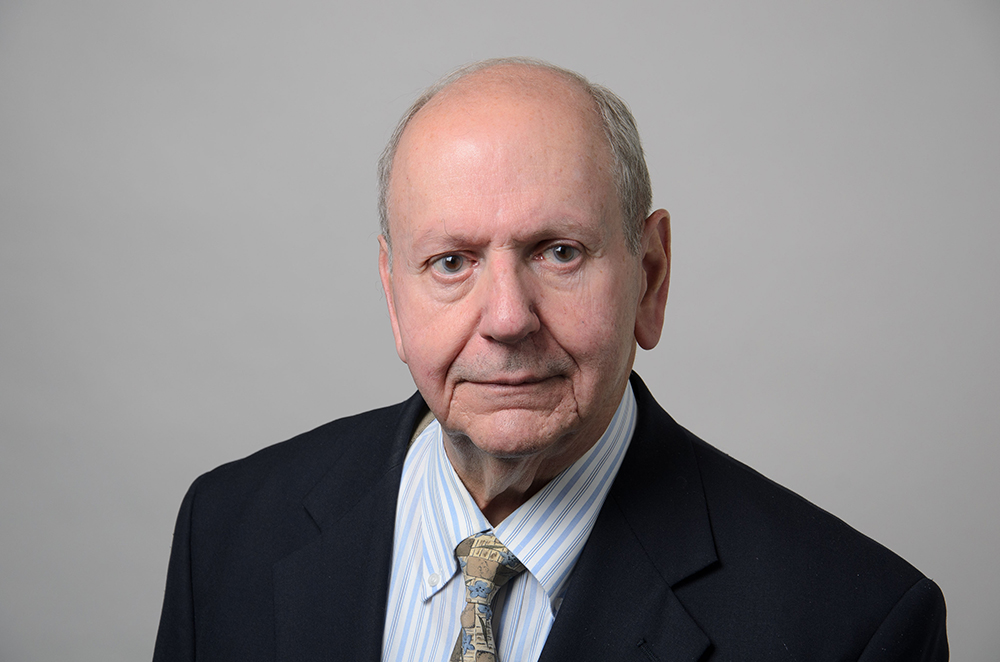 Portrait of Louis Cretella wearing a black blazer and a collared blue shirt with a tie.